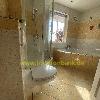 Gefliestes Badezimmer mit Duschkabine, Badewanne, Toilette und Fenster mit einer Pflanze.
