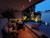 Überdachte Terrasse mit Sitzbereich, Holzdeck, Pflanzen und roten Liegestühlen neben einem gepflasterten Innenhof.