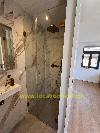 Badezimmer mit einer gläsernen Duschkabine, Wandfliesen in Marmoroptik und einem Waschbecken neben einem angrenzenden Raum.