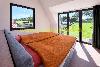 Doppelbett mit orangefarbener Bettwäsche neben großen Fenstern mit Blick auf eine grüne Landschaft.