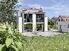 Modernes Haus mit großen Glasflächen, Terrasse und angelegtem Garten neben einem weißen Haus mit roten Dachziegeln.
