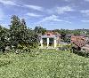 Ein Haus mit rotem Ziegeldach und großen Fenstern steht hinter einer weitläufigen grünen Gartenfläche.