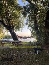 Ein hölzerner Picknicktisch steht unter Bäumen im Garten neben einer Hängematte am Wasser.