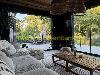 Wohnzimmer mit großem Ecksofa, hölzernem Couchtisch und bodentiefen Fenstern mit Blick auf einen Garten und eine Terrasse.