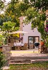 Terrasse mit einem gedeckten Esstisch unter einem Sonnenschirm, umgeben von Palmen, Kakteen und üppigem Grün.