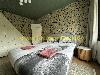 Schlafzimmer mit einem Doppelbett, botanischer Tapete, weißen Schranktüren und einem runden hölzernen Nachttisch.