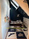 Kinderzimmer mit einem niedrigen Holzbett, einer Tier-Puzzlematte, einem Dachfenster im schrägen Dach und Büchern an der Wand.