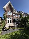 Backsteinhaus mit Giebelfront, weißen Fensterrahmen und einer Terrasse mit Gartenmöbeln.