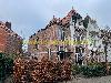Aneinandergebaute Backsteinhäuser mit roten Ziegeldächern und einer weiß verzierten Fassade hinter Hecken.