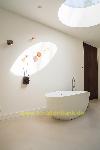 Freistehende ovale Badewanne unter einem runden Oberlicht, mit Wanddekorationen und einer dunklen Holztür.