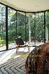 Ein Sessel und ein gemustertes Sofa stehen auf einem gestreiften Teppich, umgeben von Glaswänden mit schwarzen Rahmen.