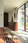Abgerundetes Sideboard aus dunklem Holz neben hohen gläsernen Schiebetüren, mit farbenfrohem gemustertem Stoff im Vordergrund.