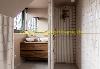 Badezimmer mit zwei Waschbecken, hölzernem Waschtischunterschrank, großem Spiegel und einer gefliesten Dusche mit Regenduschkopf.