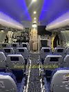 Eine Flugzeugkabine zeigt einen Mittelgang mit Reihen blauer Sitze und beleuchteten Gepäckfächern über den Passagieren.