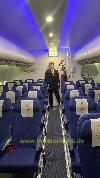 Eine Person steht im Gang einer Flugzeugkabine zwischen Reihen blauer Sitze und geöffneten Gepäckfächern.