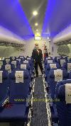 Ein Mann im Anzug steht im Gang eines Flugzeugs zwischen Reihen blauer Sitze unter blauer Beleuchtung.