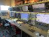 Ein langer Arbeitsplatz mit mehreren Computerbildschirmen, aufgehängten Headsets und Bürostühlen.