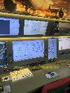Eine Bedienkonsole mit mehreren Computerbildschirmen, beleuchteten Schaltern und einem roten Stuhl.