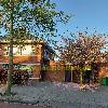 Zweigeschossiges Backsteingebäude mit geschlossenen Holztoren, Bäumen und rosa Blüten am Gehweg.