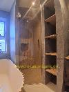 Begehbare Dusche mit Glastür, holzähnlicher Wandverkleidung und offenen Holzregalen neben einer freistehenden Badewanne.