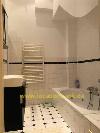 Ein gefliestes Badezimmer mit einer Badewanne, einem weißen Handtuchheizkörper und einem schwarzen Waschtischunterschrank.