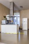Weiße Kücheninsel mit Kochfeld und Dunstabzugshaube neben einem weißen Retro-Kühlschrank und hohen Fenstern.