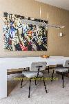 Bunte Wandkunst hängt über einem langen weißen Tisch mit Stühlen und einer länglichen Pendelleuchte.