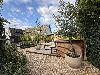 Holzterrasse mit Sitzmöbeln, Pflanzkübeln und einem grünen Garten vor einem Haus mit Satteldach.