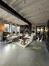 Wohnzimmer mit sichtbaren weißen Deckenbalken, Sofas, einem großen Teppich und schwarz gerahmten Glastüren.