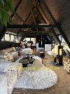 Helles Wohnzimmer unter einem schrägen Dach mit sichtbaren Holzbalken, Sitzbereich und großem Teppich.