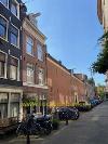 Backsteinfassaden säumen eine schmale Straße mit abgestellten Fahrrädern und Bäumen unter einem klaren blauen Himmel.