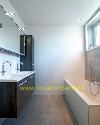 Badezimmer mit Doppelwaschbecken, dunklen Waschtischunterschränken, weißen Wandfliesen und einer Badewanne am Fenster.