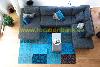 Ein graues Ecksofa steht um einen blauen Patchworkteppich mit einem hellen Couchtisch.