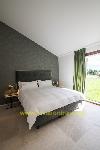 Ein Schlafzimmer mit einem bezogenen Doppelbett vor einer dunklen Strukturtapete und grünen Vorhängen neben einem großen Fenster.