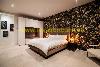 Schlafzimmer mit einem großen Bett, dunkler botanischer Tapete, weißen Schränken und warmer Beleuchtung.